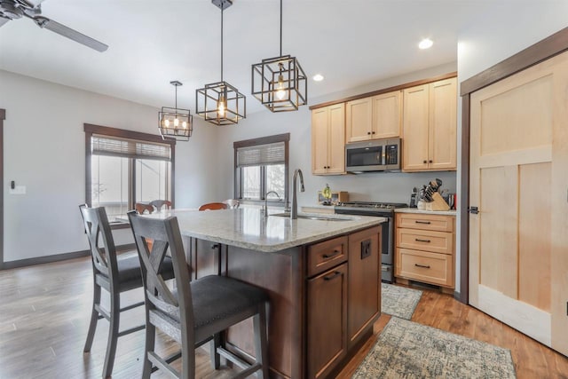 kitchen with pendant lighting, light brown cabinets, a center island with sink, sink, and appliances with stainless steel finishes