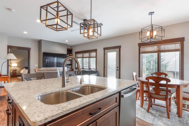 kitchen featuring sink, a healthy amount of sunlight, an inviting chandelier, stainless steel dishwasher, and a kitchen island with sink