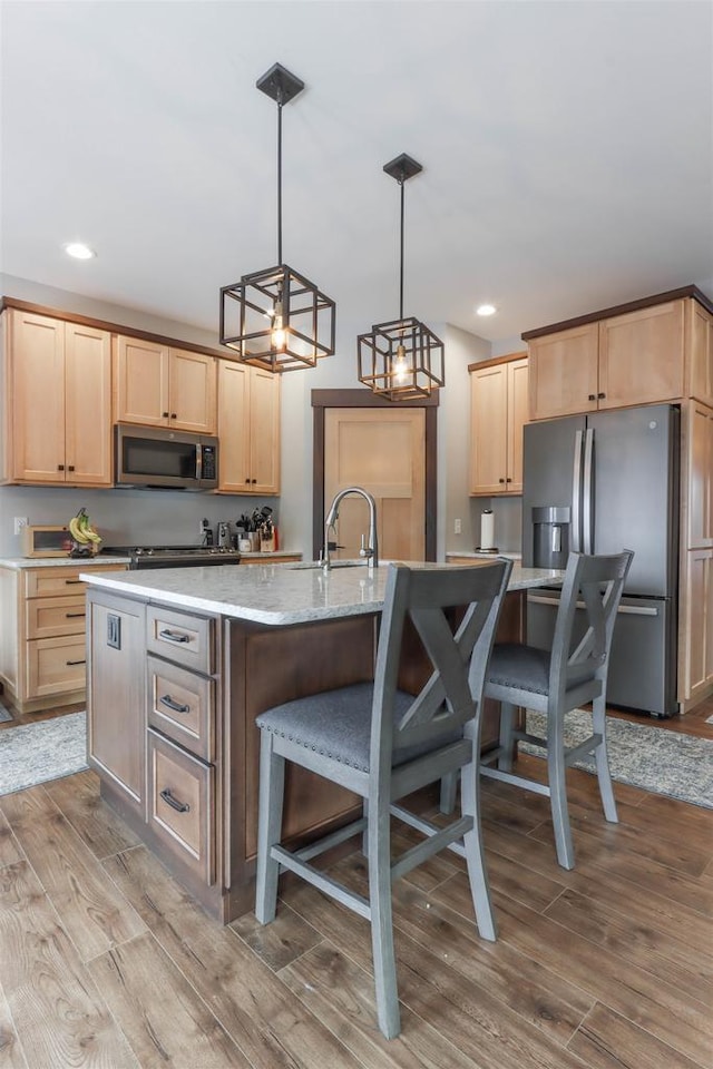 kitchen featuring appliances with stainless steel finishes, a center island with sink, hanging light fixtures, and light brown cabinetry