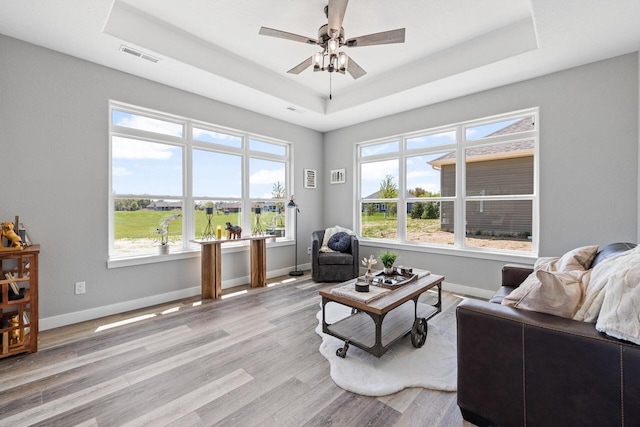 living room with a tray ceiling, visible vents, and baseboards