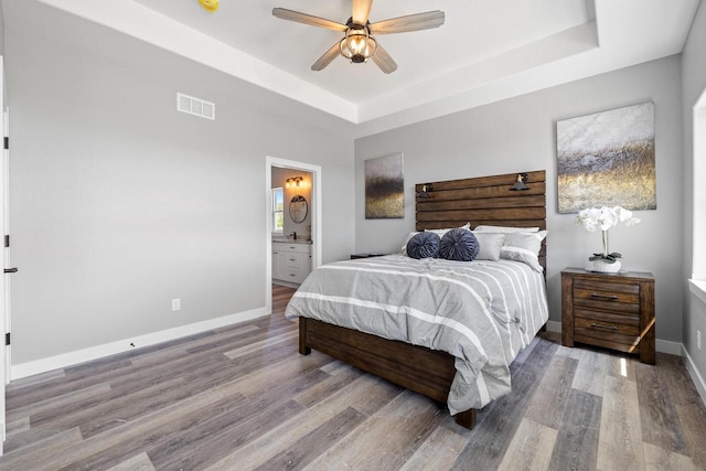 bedroom with a raised ceiling, visible vents, baseboards, and wood finished floors