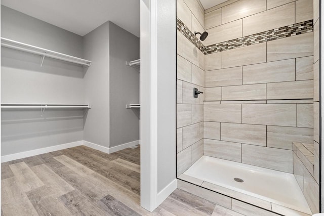 full bath featuring a spacious closet, wood finished floors, a shower stall, and baseboards