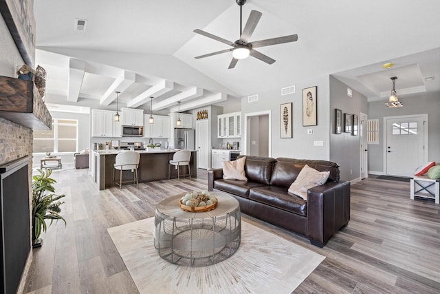 living area with lofted ceiling, visible vents, light wood-style floors, a brick fireplace, and baseboards