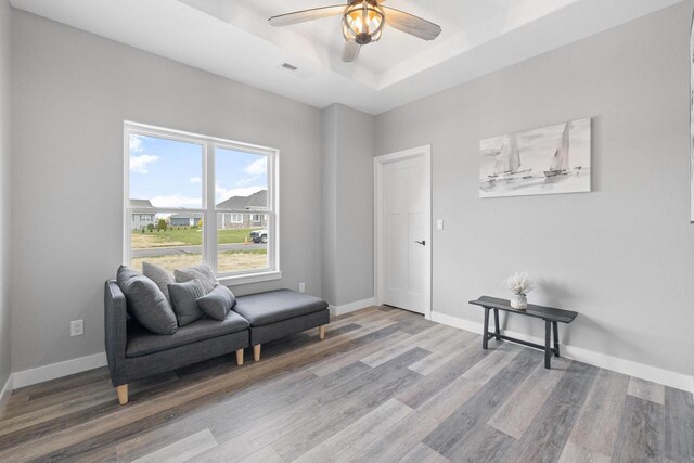 living area with ceiling fan, light wood-style flooring, visible vents, baseboards, and a raised ceiling