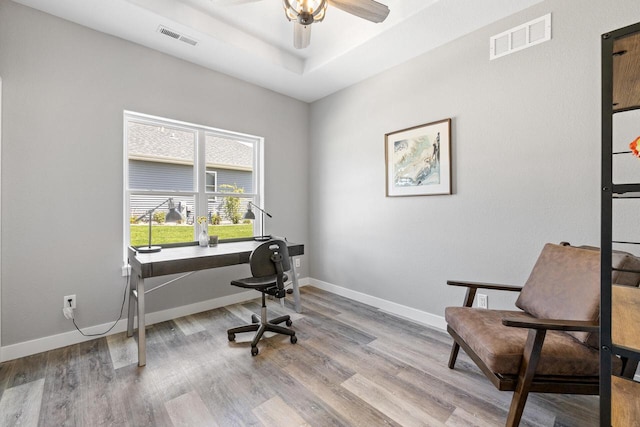 office featuring a tray ceiling, light wood finished floors, visible vents, and baseboards