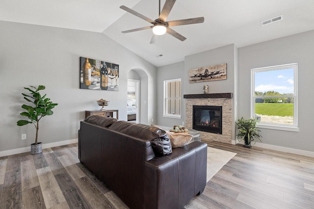 living area featuring baseboards, visible vents, a glass covered fireplace, lofted ceiling, and wood finished floors