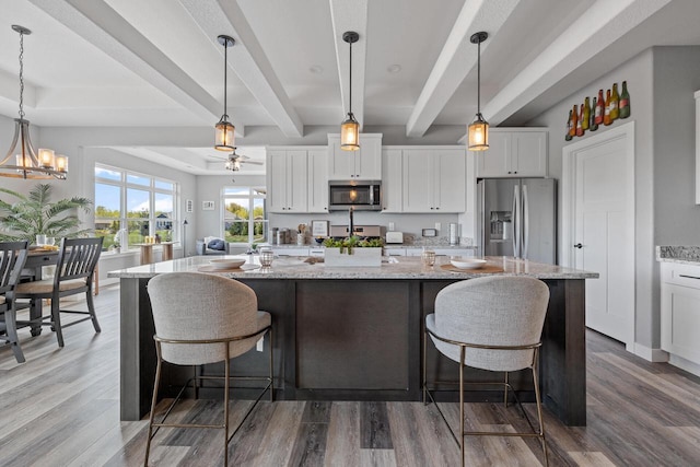 kitchen with light stone counters, appliances with stainless steel finishes, hanging light fixtures, and white cabinetry