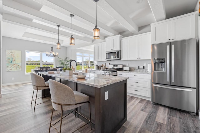 kitchen featuring a center island with sink, appliances with stainless steel finishes, white cabinets, and light stone counters