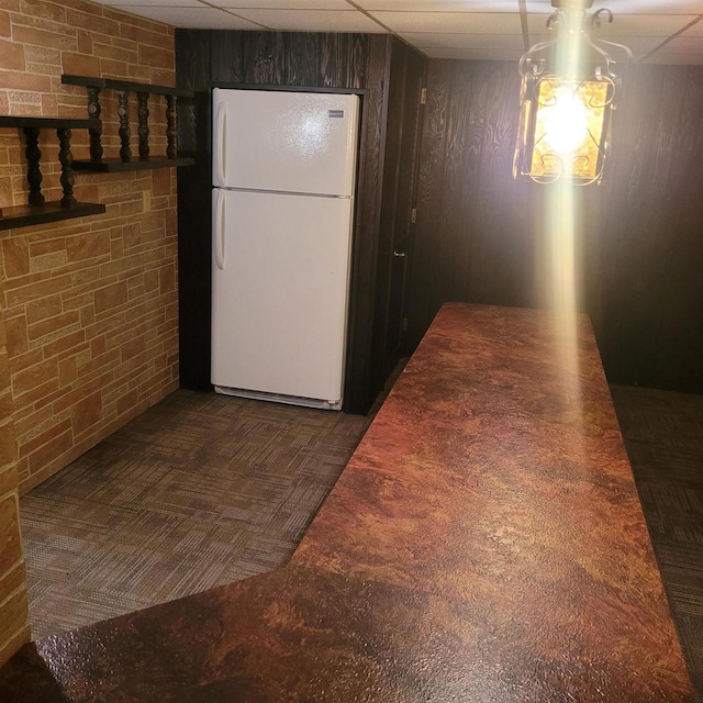 kitchen featuring a paneled ceiling, dark brown cabinets, wood walls, and white fridge