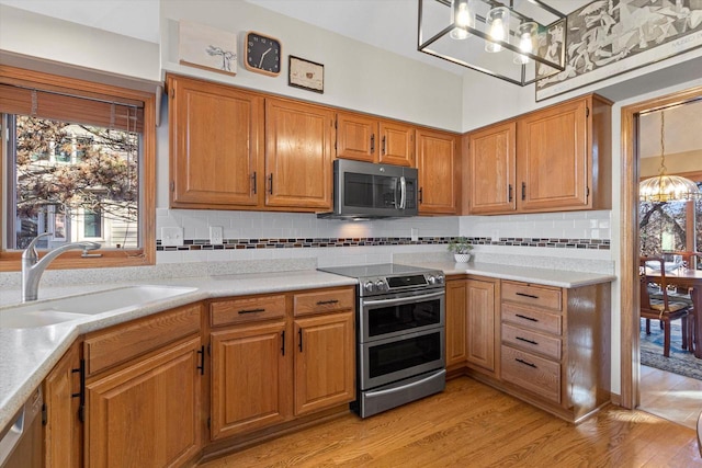 kitchen featuring sink, an inviting chandelier, decorative backsplash, appliances with stainless steel finishes, and light wood-type flooring