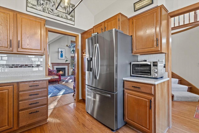 kitchen with decorative backsplash, stainless steel fridge, light wood-type flooring, and vaulted ceiling