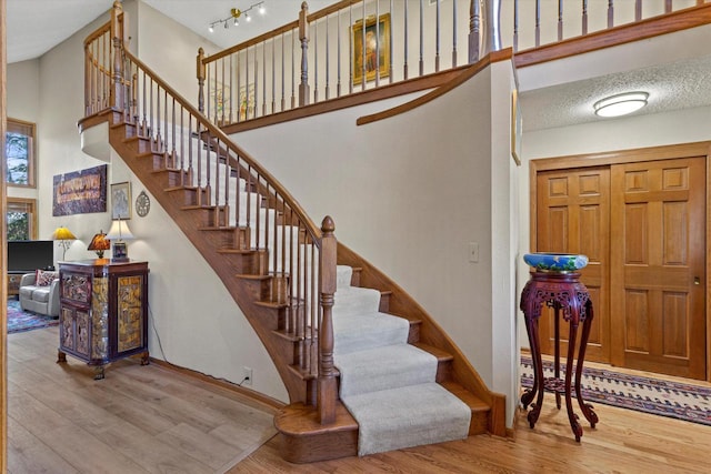 staircase featuring wood-type flooring, a textured ceiling, and a high ceiling