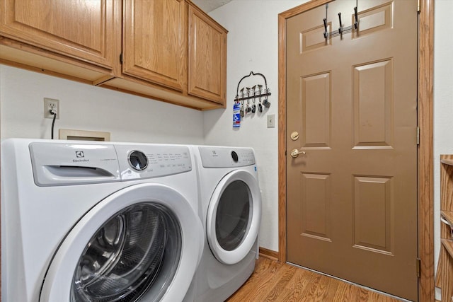 clothes washing area featuring washer and clothes dryer, cabinets, and light wood-type flooring