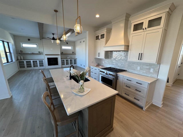 kitchen featuring high end stainless steel range oven, custom range hood, ceiling fan, and an island with sink