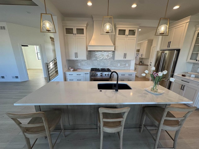 kitchen featuring sink, an island with sink, custom exhaust hood, pendant lighting, and appliances with stainless steel finishes