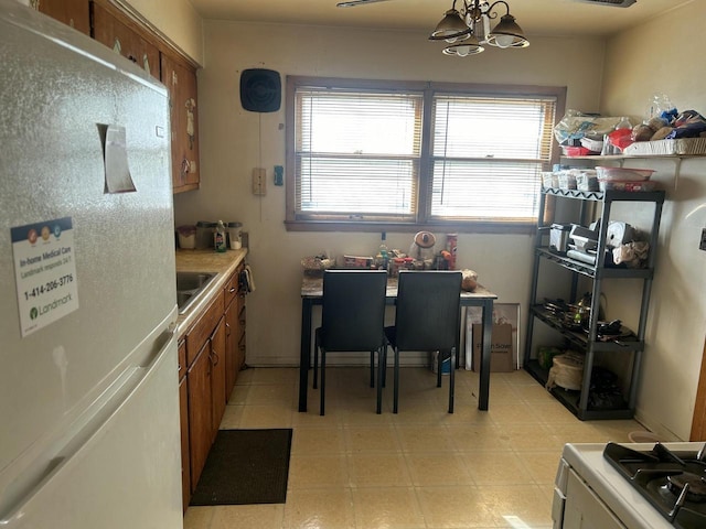 kitchen with sink, hanging light fixtures, white refrigerator, a chandelier, and range