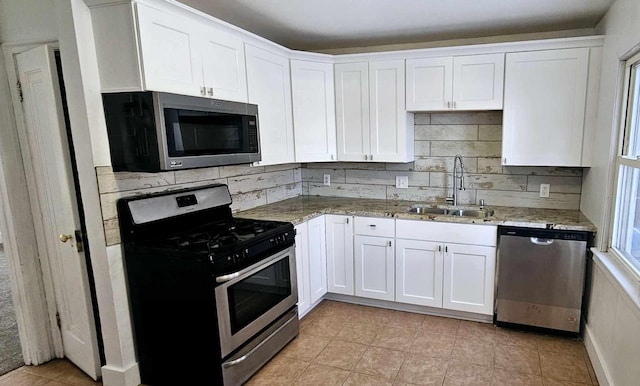 kitchen with white cabinetry, sink, light stone countertops, light tile patterned floors, and appliances with stainless steel finishes