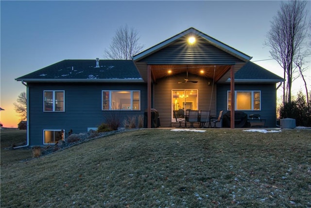 back house at dusk with ceiling fan, a patio area, and a yard