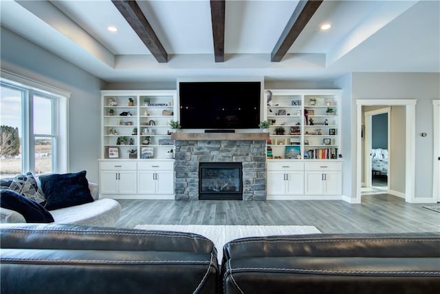 living room with light hardwood / wood-style floors, a stone fireplace, and beam ceiling