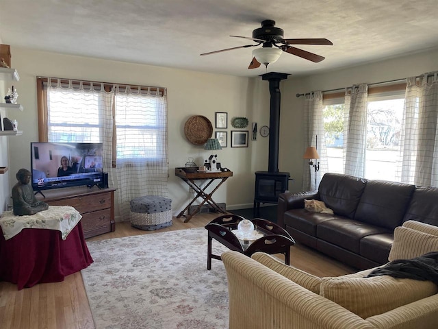 living room with light hardwood / wood-style floors, a wood stove, and ceiling fan