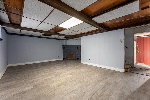 unfurnished living room featuring a paneled ceiling, a brick fireplace, and light wood-type flooring