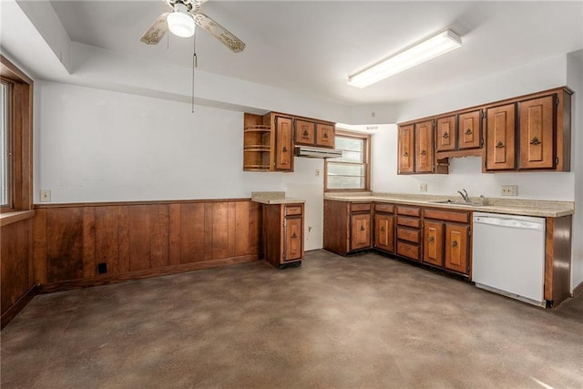 kitchen featuring dishwasher, wood walls, concrete floors, ceiling fan, and sink