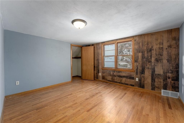 empty room with a textured ceiling, wood walls, and light hardwood / wood-style floors