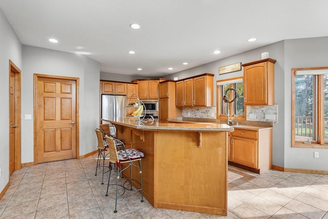 kitchen with a kitchen island with sink, appliances with stainless steel finishes, light tile patterned floors, a kitchen bar, and tasteful backsplash