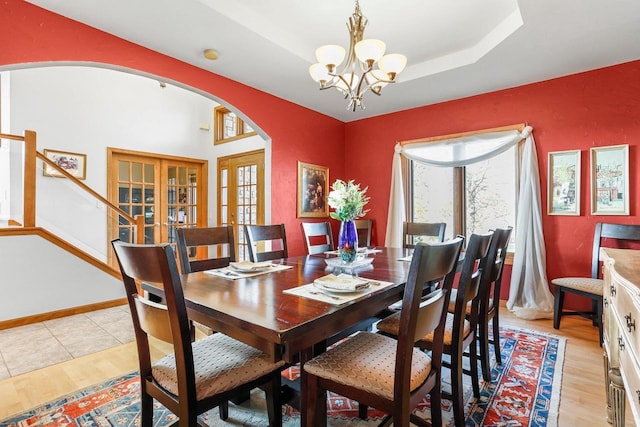 dining room with french doors, a raised ceiling, an inviting chandelier, and light wood-type flooring