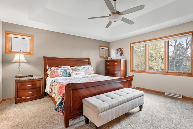 carpeted bedroom with ceiling fan and a tray ceiling