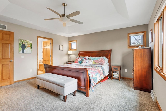 carpeted bedroom featuring ceiling fan, ensuite bath, and a tray ceiling