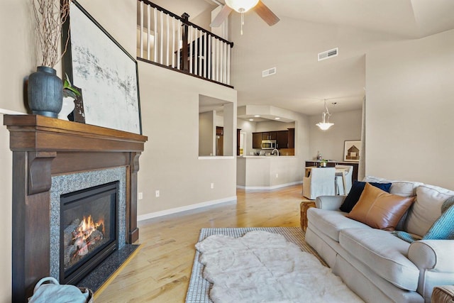 living room with light hardwood / wood-style floors, ceiling fan, high vaulted ceiling, and a tiled fireplace