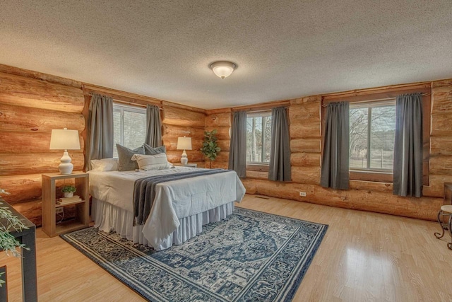 bedroom with a textured ceiling, log walls, and hardwood / wood-style flooring