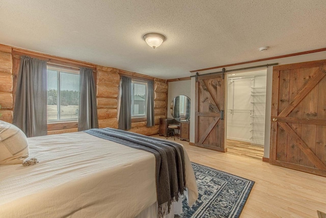 bedroom featuring log walls, a textured ceiling, a barn door, and wood-type flooring