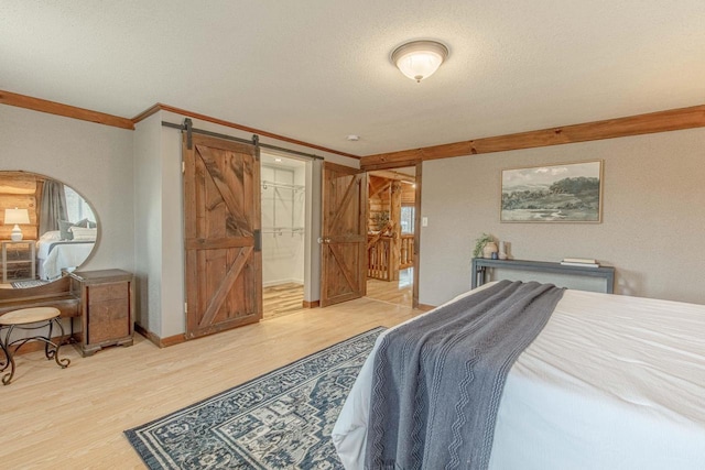 bedroom with hardwood / wood-style flooring, a textured ceiling, a spacious closet, a barn door, and crown molding