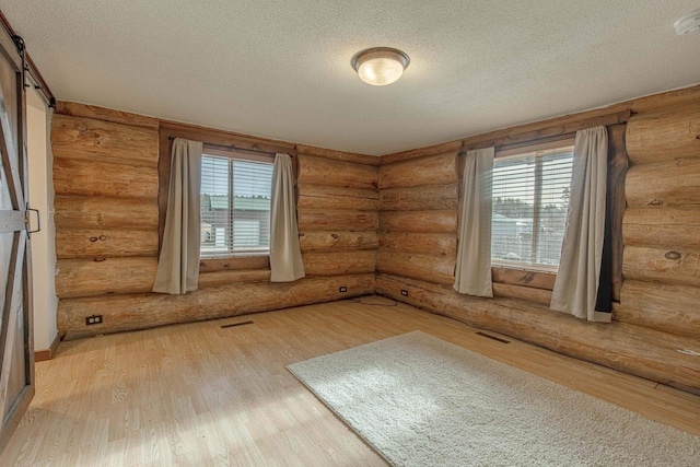 empty room with a textured ceiling, rustic walls, hardwood / wood-style flooring, a healthy amount of sunlight, and a barn door