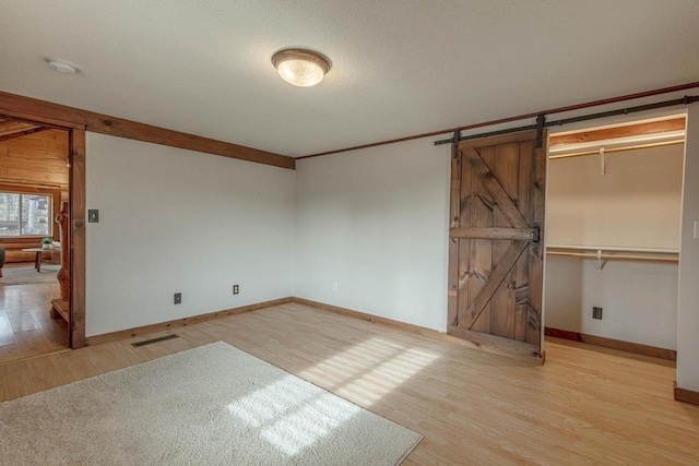 unfurnished bedroom featuring crown molding, a barn door, light hardwood / wood-style flooring, and a closet