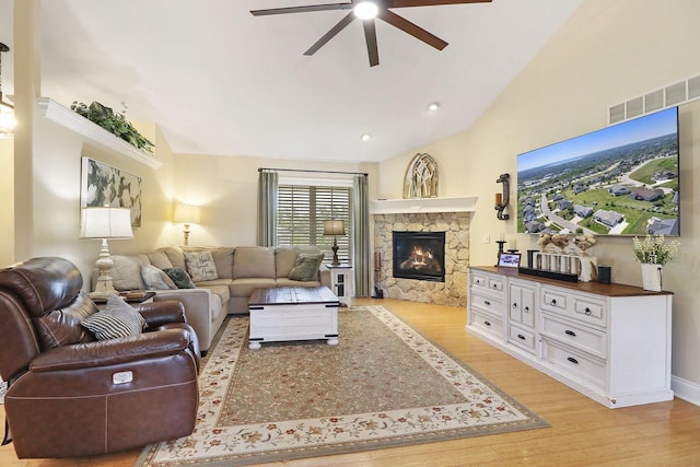 living room featuring ceiling fan, light wood-type flooring, a stone fireplace, and lofted ceiling