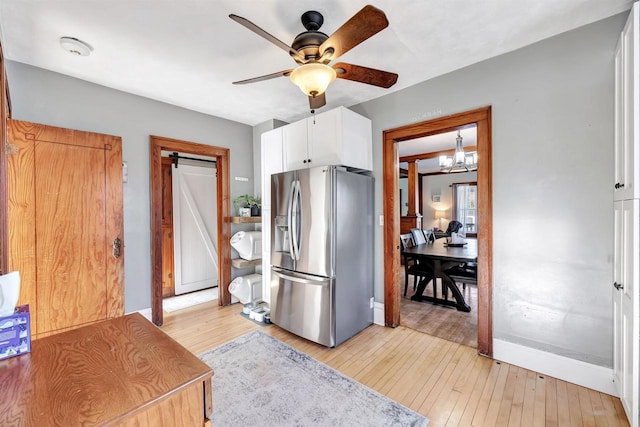 kitchen with stainless steel fridge with ice dispenser, light wood-type flooring, a barn door, white cabinetry, and ceiling fan with notable chandelier