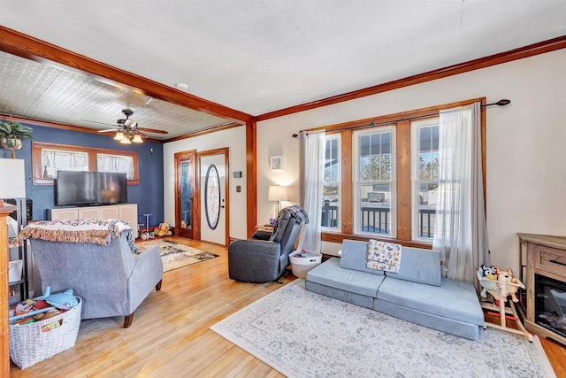 living room featuring ceiling fan, crown molding, light wood-type flooring, and a wealth of natural light