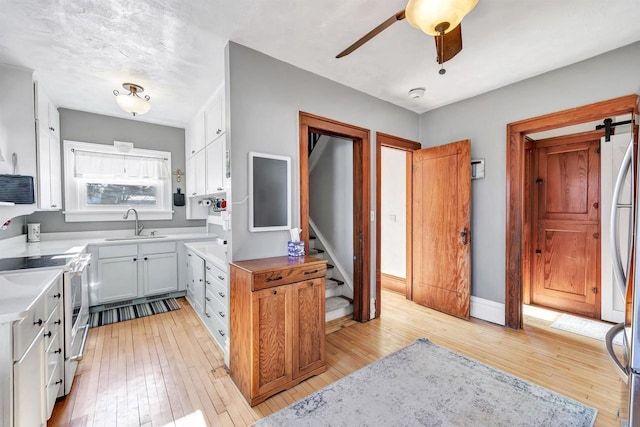 kitchen with white electric stove, light hardwood / wood-style floors, ceiling fan, white cabinets, and sink