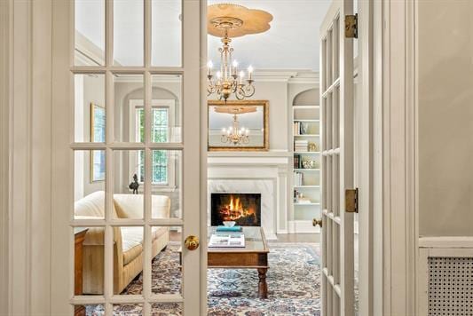 living area with radiator heating unit, a high end fireplace, french doors, a chandelier, and crown molding