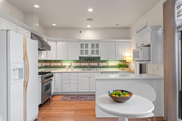 kitchen featuring white cabinetry, white appliances, light wood-type flooring, wall chimney exhaust hood, and sink