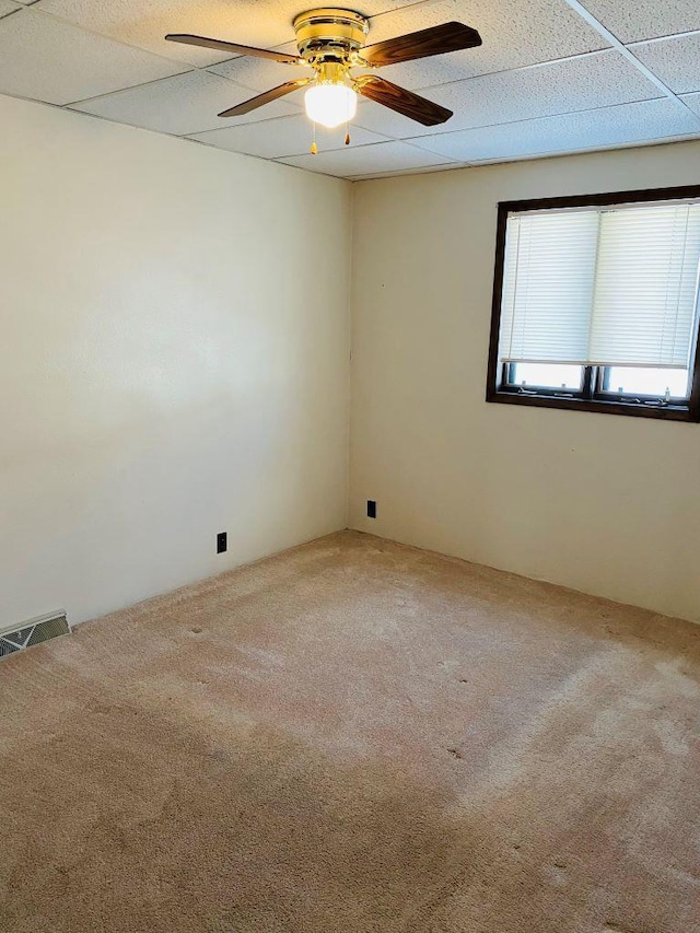 carpeted empty room with ceiling fan and a drop ceiling