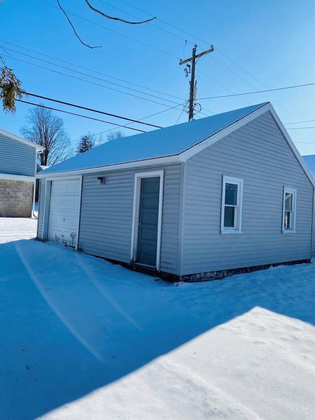 view of snowy exterior with a garage and an outbuilding