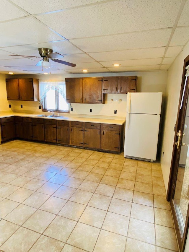 kitchen with ceiling fan, white refrigerator, a drop ceiling, sink, and light tile patterned flooring