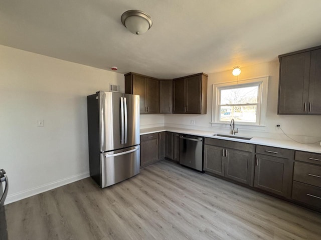 kitchen featuring light wood-type flooring, appliances with stainless steel finishes, dark brown cabinets, and sink