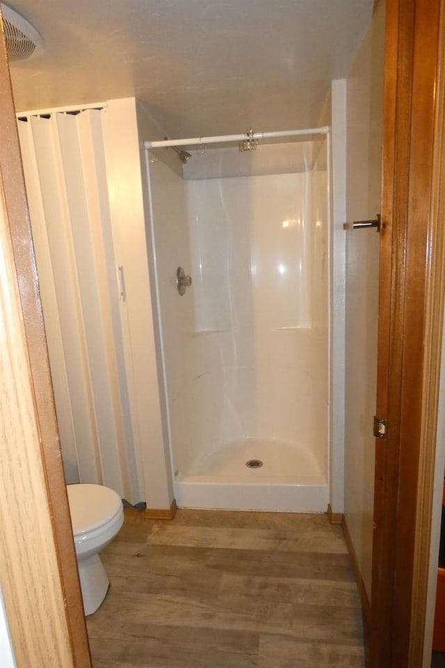 bathroom featuring walk in shower, toilet, and hardwood / wood-style flooring