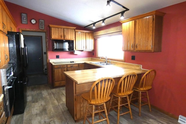 kitchen featuring sink, lofted ceiling, kitchen peninsula, black appliances, and dark wood-type flooring