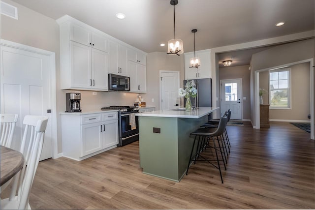 kitchen with stainless steel range with gas stovetop, black refrigerator, hanging light fixtures, a center island, and white cabinets